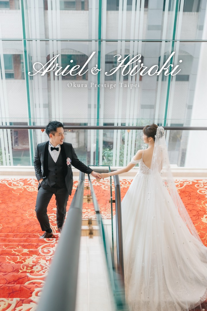 新郎新娘在台北大倉久和大飯店紅毯樓梯牽手對望，上方寫著 Ariel & Hiroki Okura Prestige Taipei｜台北婚攝